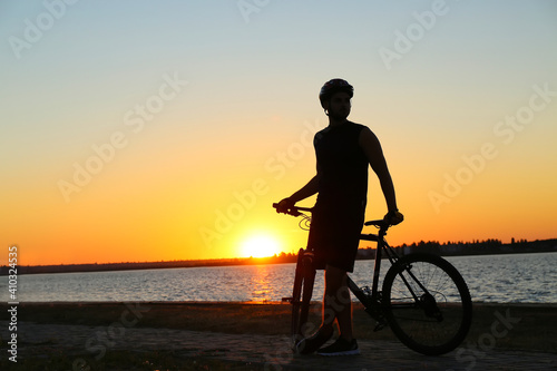 Silhouette of male cyclist with bicycle against sunset