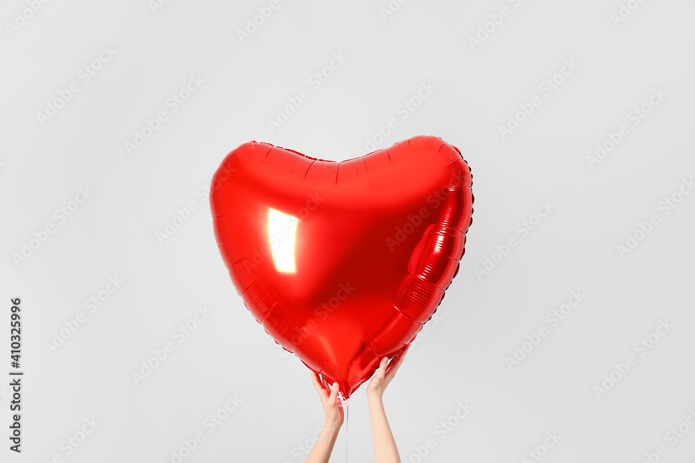 Female hands with heart shaped air balloon on grey background Female hands with heart shaped air balloon on grey background