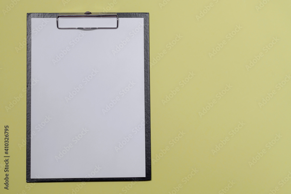 A black folder with a clip and attached white sheet on an isolated yellow background. Mockup for your text A black folder with a clip and attached white sheet on an isolated yellow background. Mockup for your text