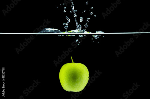 Green apple falling in water with a splash against dark background