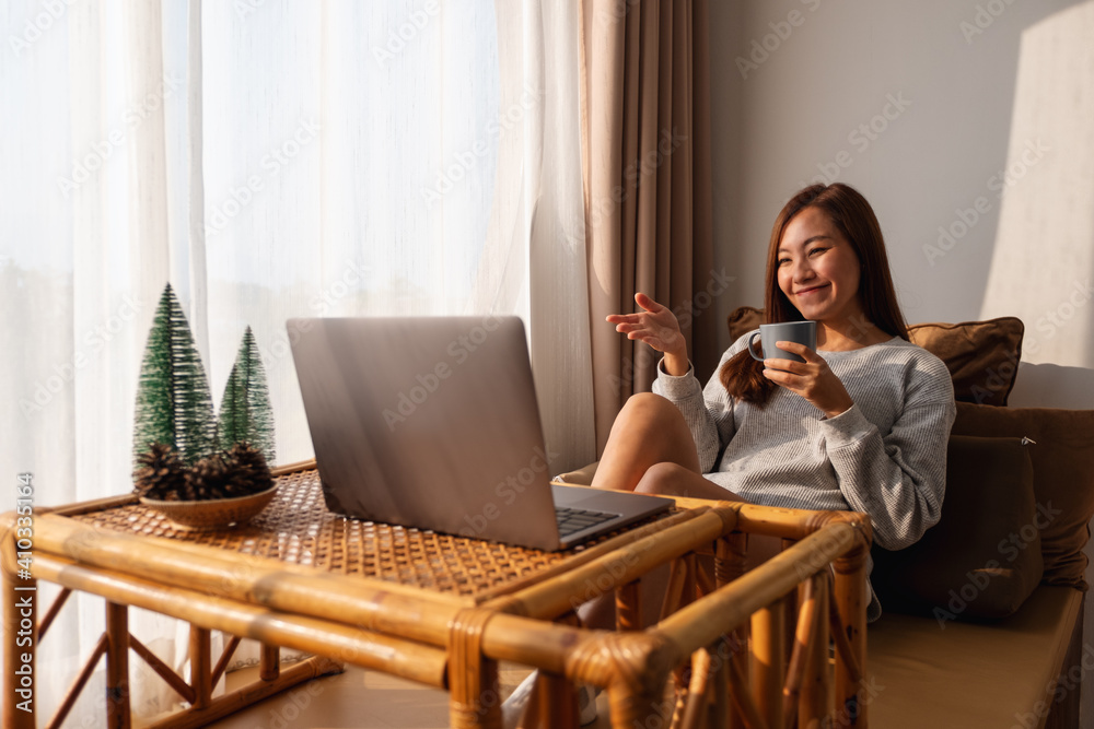 A beautiful young asian woman using laptop computer for video call while sitting and drinking coffee at home A beautiful young asian woman using laptop computer for video call while sitting and drinking coffee at home