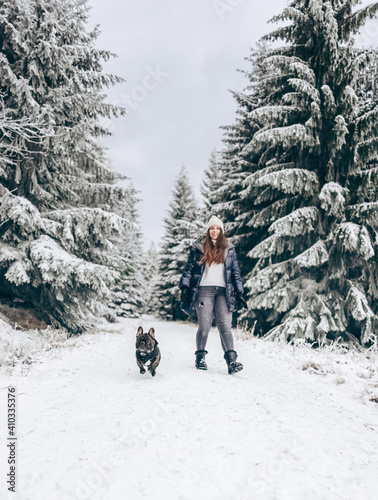 Front view of a girl walking her dog in the park through a snow-covered pine forest in winter.Hiking with your best friend.Winter lifestyle. reconnecting with nature.local travel