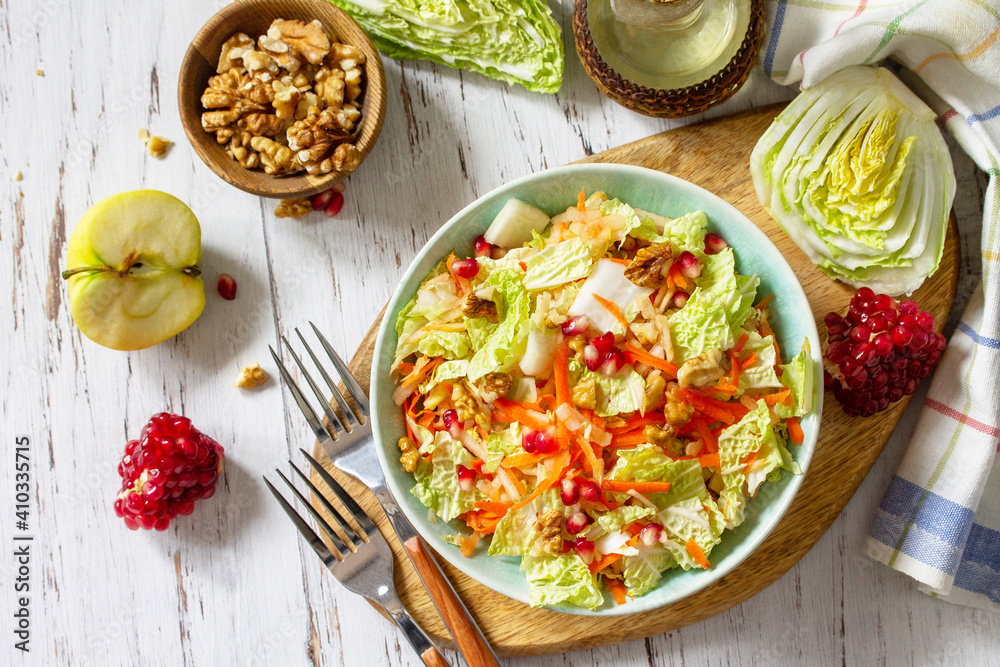 Dietary salad fresh vegetable of Chinese cabbage, carrots, apple, nuts and pomegranate with vinaigrette dressing on a white wooden table. Top view flat lay. Dietary salad fresh vegetable of Chinese cabbage, carrots, apple, nuts and pomegranate with vinaigrette dressing on a white wooden table. Top view flat lay.