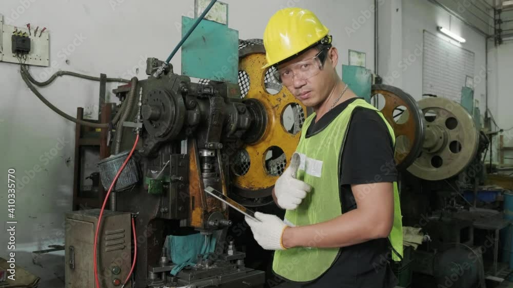 An Asian male engineer is inspecting and repairing machines in the factory. Then raise his thumb to show confidence. industrial and engineering concept. An Asian male engineer is inspecting and repairing machines in the factory. Then raise his thumb to show confidence. industrial and engineering concept.