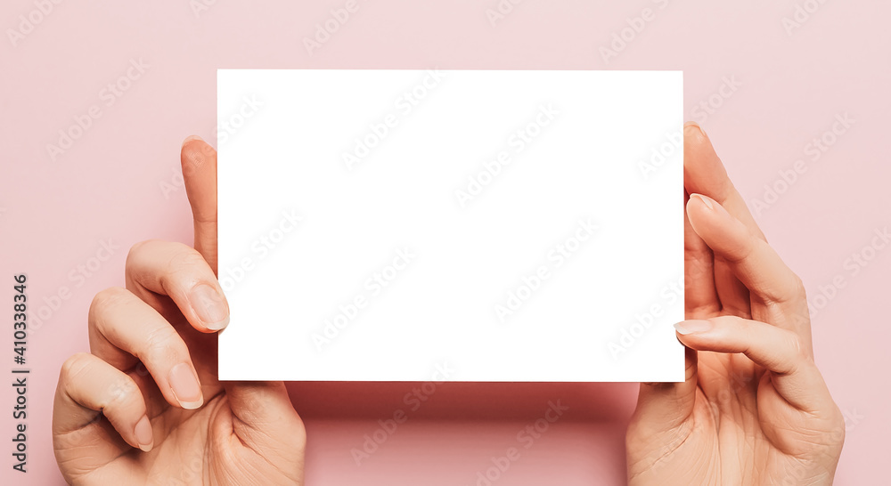 Female hands hold a blank sheet of paper on a pink background. Advertising space - obrazy, fototapety, plakaty 