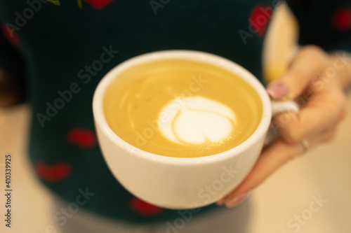 Close up of beautiful female hands holding big white cup of cappuccino coffee. Selective focus.
