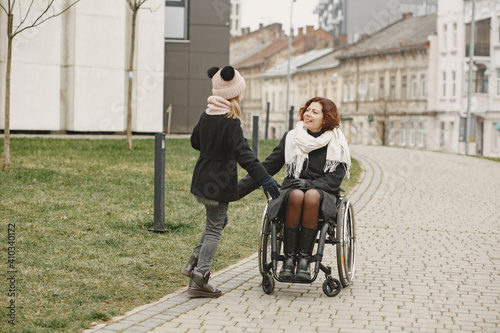 Disabled woman in wheelchair with daughter. Family walking outside at park.