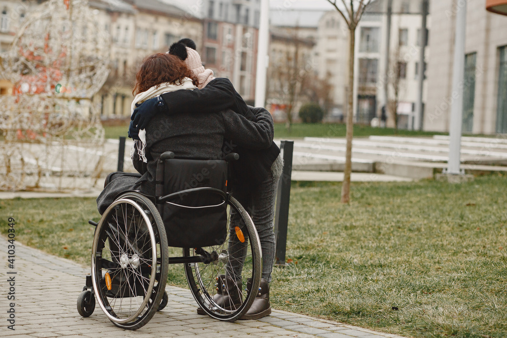 Obraz premium Disabled woman in wheelchair with daughter. Family walking outside at park.