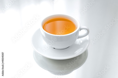 A horizontal photo of a white porcelain cup of green tea on a saucer, on a mirror table, a reflection
