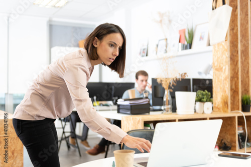Fotografie Serious hispanic woman spying the laptop of her coworker in the office