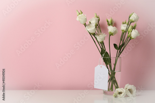 Vase with roses and blank tag against pink background