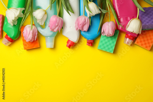 Detergents, sponges and tulips on yellow background