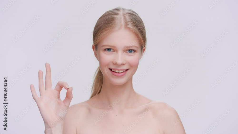 Young blonde woman makes an ok sign, looks at the camera and smiles Young blonde woman makes an ok sign, looks at the camera and smiles