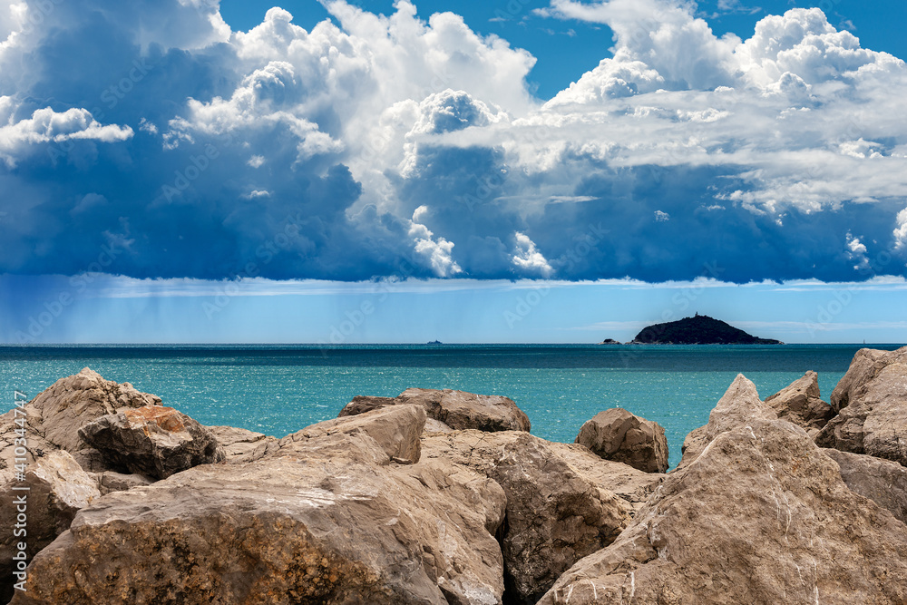 Cumulus clouds (cumulonimbus) on blue sky with torrential rain over the Mediterranean sea with breakwater in foreground. Liguria, Italy, Europe.
