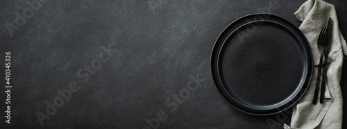 Empty black plates with black cutlery and gray napkin on black table. Top view, banner for website.