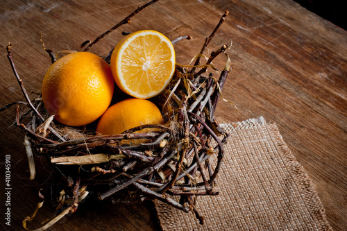 Ripe yellow lemons in a wicker basket in the shape of a bird's nest, lying on an old wooden surface.