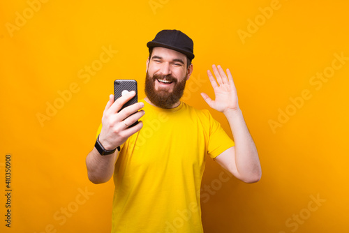 Cheerful young bearded man is talking with someone on video call .
