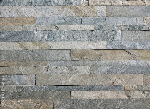 Wall cladding for exterior made of natural stones strips with different sizes. Colors are gray and light brown. Background and texture