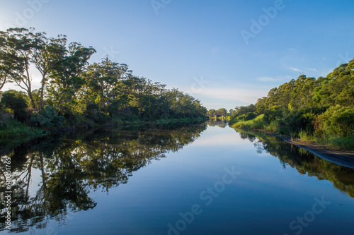 Calm river flowing among trees towards a bridge with beautiful reflections at sunset