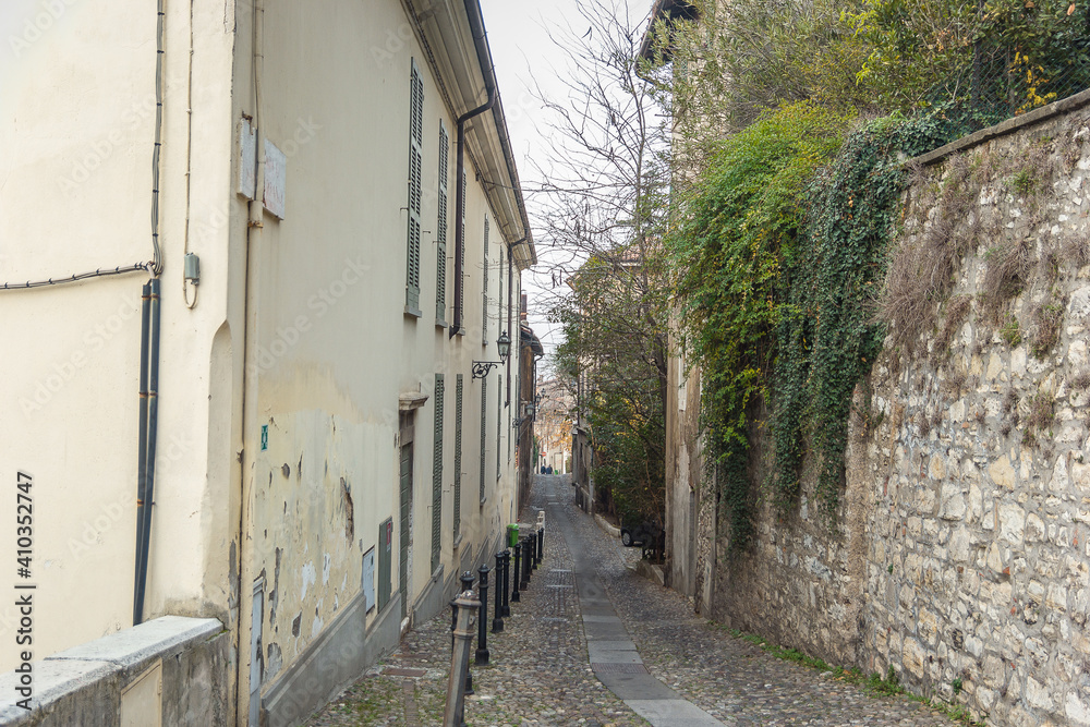 Beautiful narrow alley with many windows and green ivy on the stone wall in Brescia city. Historical architecture of the Lombardia region in Italy. Winter journey in North Italy. Travelling Europe. 