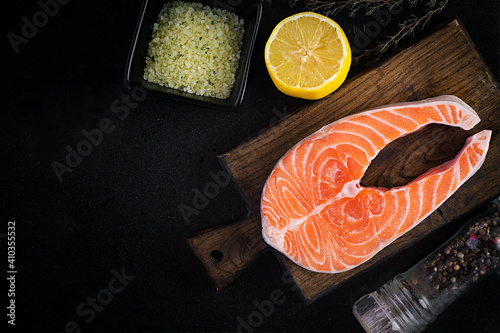 Salmon. Raw fish salmon steak fillet with cooking ingredients, herbs and lemon on black background with copy space. Top view, overhead, copy space.