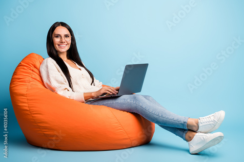Full length profile portrait of pretty person sit soft chair hold laptop eyewear isolated on blue color background