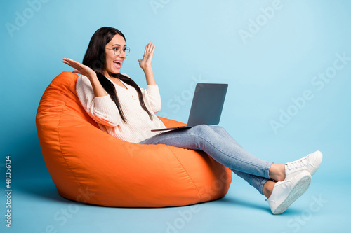 Full body profile portrait of astonished lady sit soft chair speak video chat isolated on blue color background