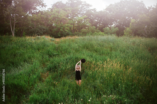 Blonde hipster girl in black dress and hat staning in the green meadow on summer day. photo