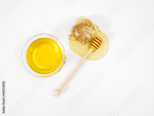 Natural fresh flower honey in bowl and wooden honey dipper on flowing honey drop with bee honeycomb on white background  top view  flat lay