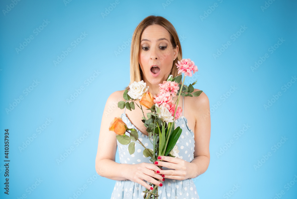 Portrait of a beautiful young woman holding big bouquet of flowers isolated over blue background.