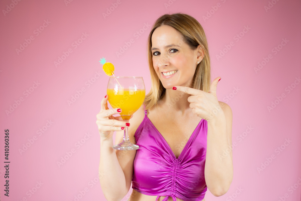 Young beautiful blonde woman drinking glass of healthy orange juice over pink background Young beautiful blonde woman drinking glass of healthy orange juice over pink background