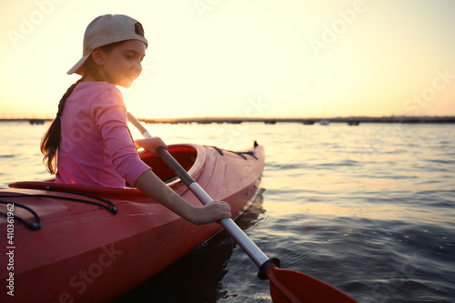 Happy girl kayaking on river at sunset. Summer camp activity