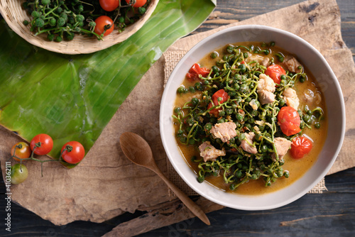 Northern Thai food (Kaeng Sa Lae), Spicy soup Broussonetia Kurzii with pork and tomatoes in a bowl on wooden background, Seasonal food in North Thailand photo