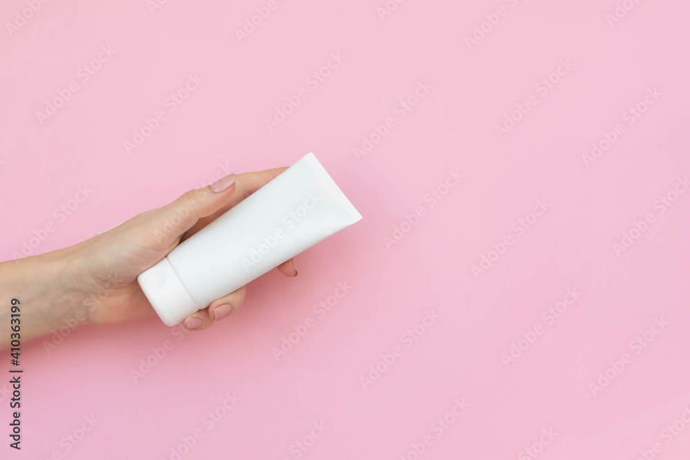 female hand holding white cosmetic tube on pink background. concept of cosmetic product for sensitive skin. Copy space
