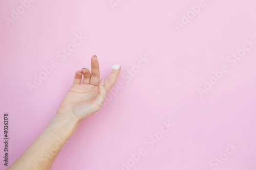 a woman's hand with a drop of cream on a pink background. Copy space