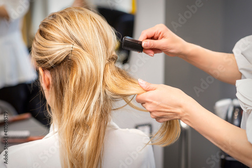 Rear View of a hairdresser combs blonde hair of the young woman in a beauty salon