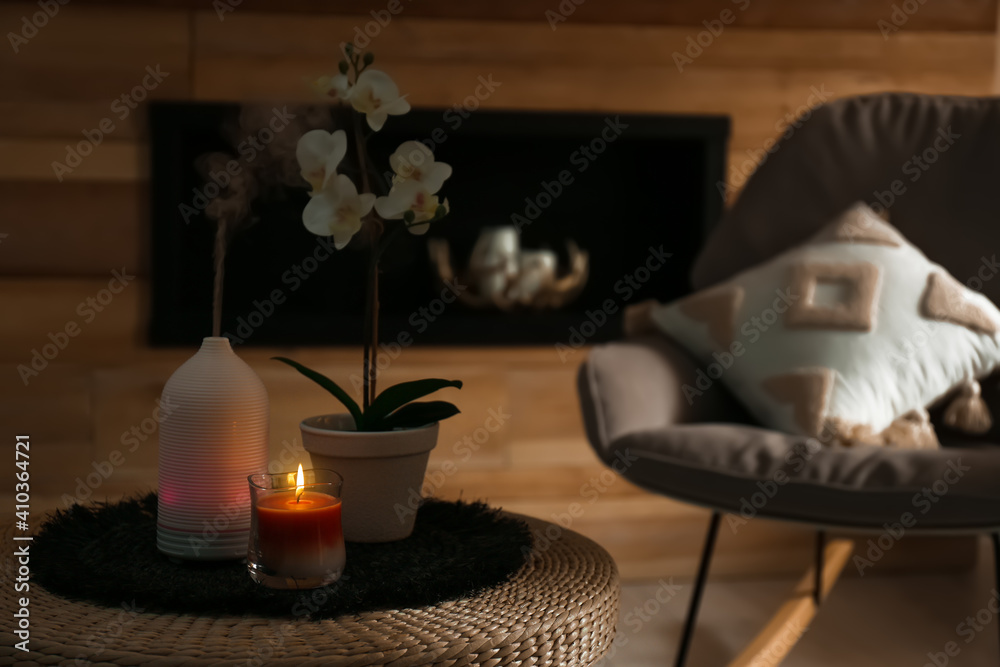 Aroma oil diffuser, burning candle and beautiful potted orchid flower on table in living room. Space for text