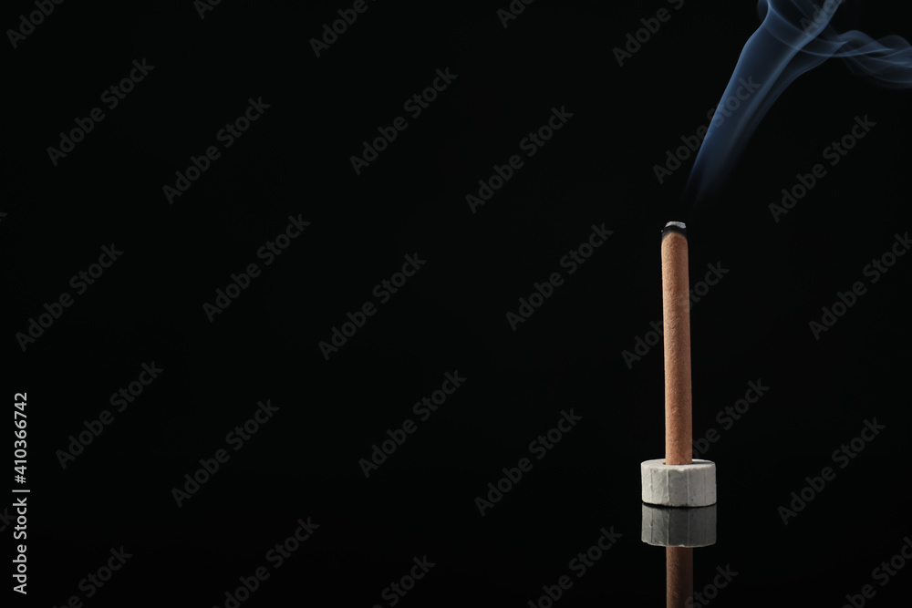 Incense stick smoldering in holder on black background. Space for text Incense stick smoldering in holder on black background. Space for text