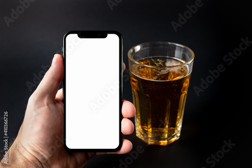 A smartphone in a man's hand and a beer on a black background.