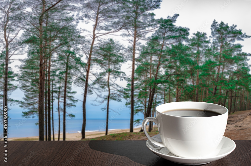 Cup of coffee on the table with view of coniferous forest and blue sea