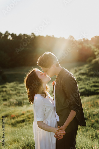 Young beautiful woman and man hug, kiss and walk in nature at sunset.
