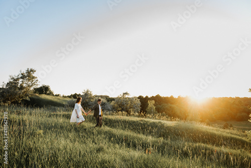 Young beautiful woman and man hug, kiss and walk in nature at sunset.