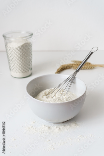 Mehl und ein Schneebesen in einer Schüssel auf einem weißen Küchentisch. Vorbereitung, backen, Frühstück.