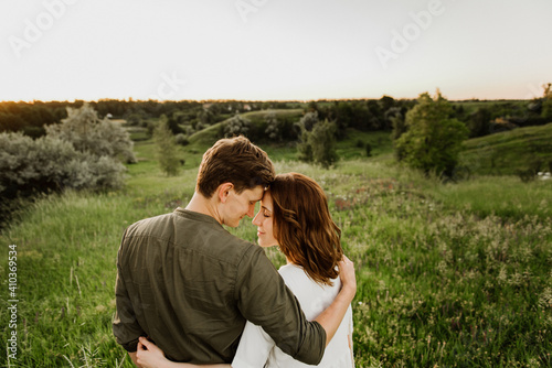 Young beautiful woman and man hug, kiss and walk in nature at sunset.