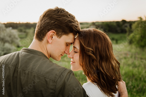 Young beautiful woman and man hug, kiss and walk in nature at sunset.