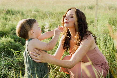 Little boy and mom are holding a dandelion in their hands on the field.