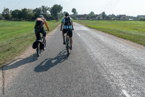 Fototapeta Naklejka Na Ścianę i Meble -  Grodno, Belarus, 16 July 2020: Two cyclists ride on an asphalt road. Cycling around the countryside. Cycling as a way of spending time and a healthy lifestyle.