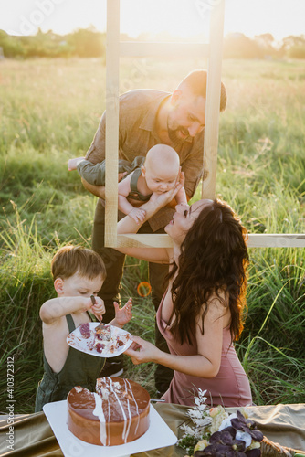 Young parents with two young sons cut and eat cake in nature.