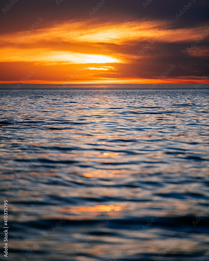 Obraz premium Low angle view looking out to a calm sea as the sun sets.