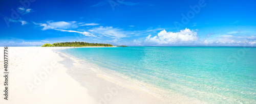 Sand spit of tropical island receding into distance. Fine sunny summer day. Sky with light clouds merges with clear water. Beauty of environment. Ultrawide format.